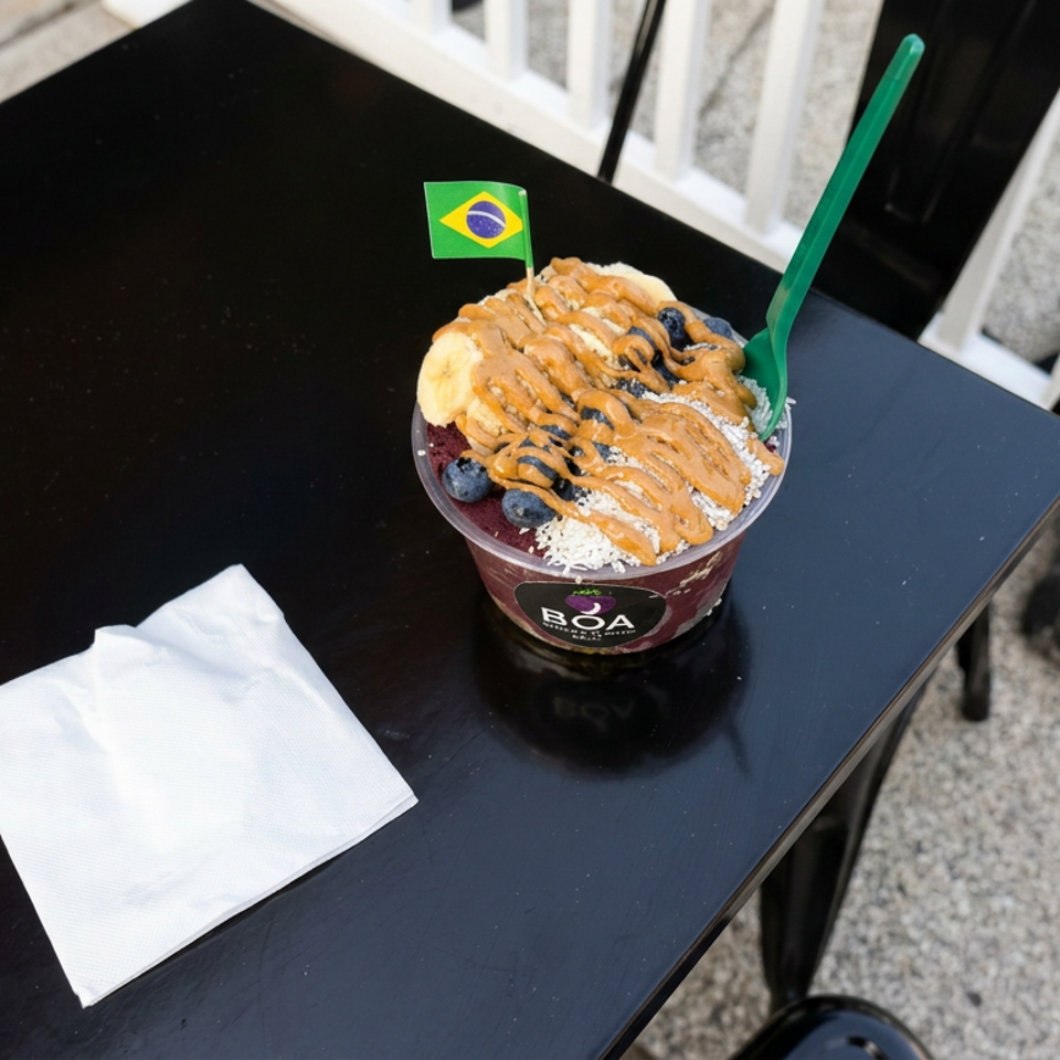 Brazilian açaí bowl topped with banana, blueberries, coconut, and peanut butter drizzle on a black table.