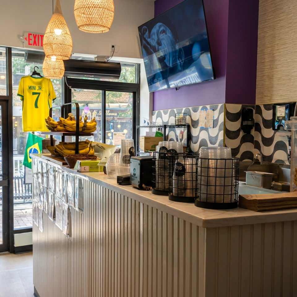 Bright BCA Brazil’s Bowls Açaí counter with bananas, toppings, patterned walls, woven pendant lights, and a hanging soccer jersey.