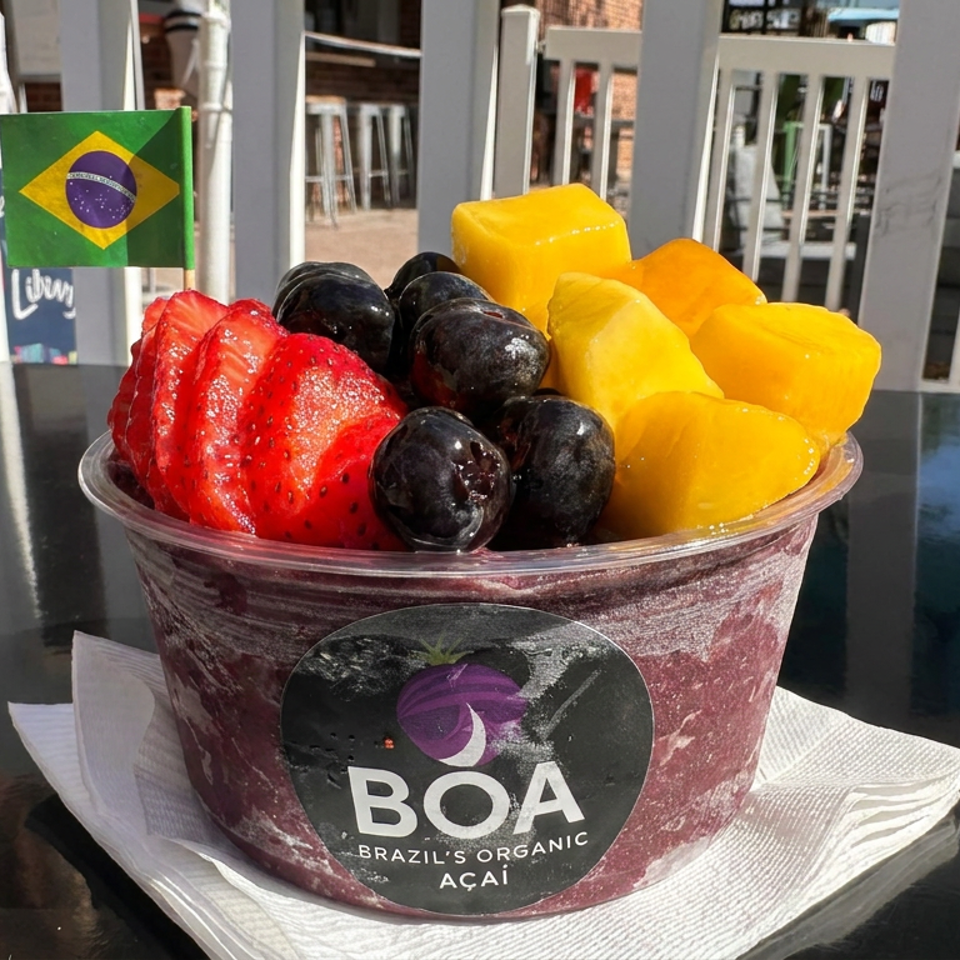 A Brazilian açaí bowl topped with strawberries, blueberries, and mango sits on a table beside a Brazilian flag.